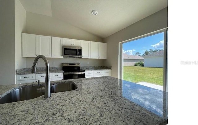 kitchen featuring light stone countertops, vaulted ceiling, stainless steel appliances, white cabinetry, and a sink