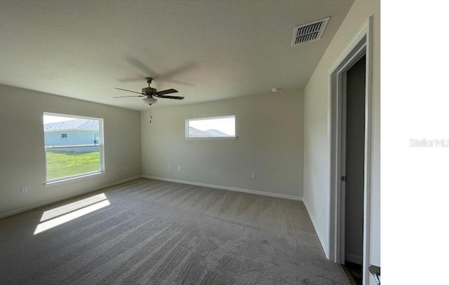 carpeted spare room featuring a ceiling fan, visible vents, and baseboards