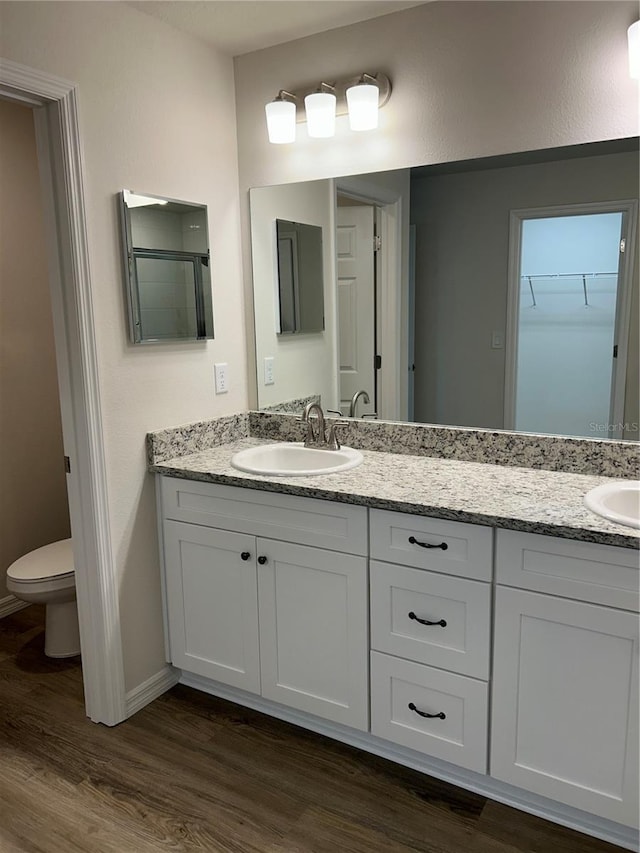 bathroom featuring double vanity, a spacious closet, toilet, a sink, and wood finished floors