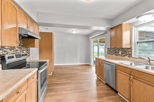 kitchen featuring sink, a textured ceiling, backsplash, stainless steel appliances, and light wood-type flooring