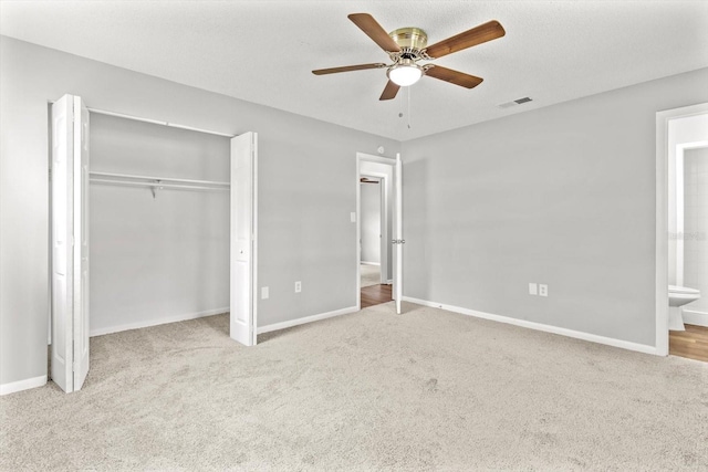 unfurnished bedroom with ceiling fan, light colored carpet, a closet, and ensuite bath