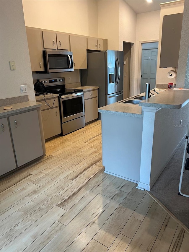 kitchen with kitchen peninsula, sink, light hardwood / wood-style flooring, and stainless steel appliances