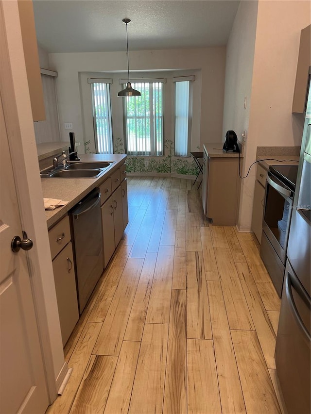 kitchen with stainless steel appliances, hanging light fixtures, sink, and light hardwood / wood-style flooring