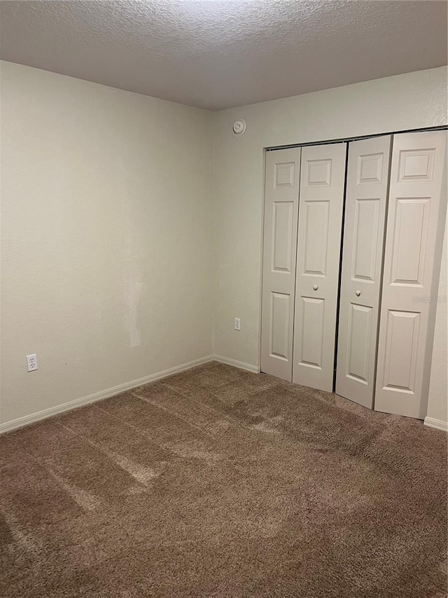 unfurnished bedroom with a textured ceiling, carpet flooring, and a closet