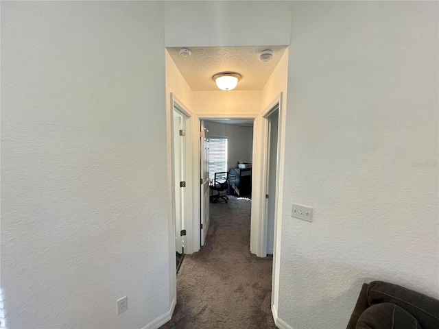 hall with dark carpet and a textured ceiling