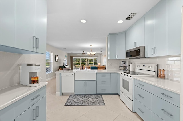 kitchen with sink, kitchen peninsula, white appliances, a chandelier, and decorative backsplash