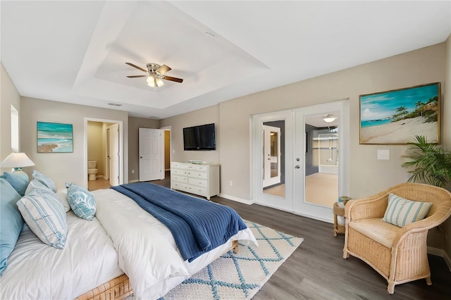 bedroom with french doors, ceiling fan, connected bathroom, a tray ceiling, and dark hardwood / wood-style flooring