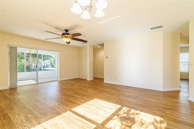 empty room featuring ceiling fan with notable chandelier and light wood-type flooring