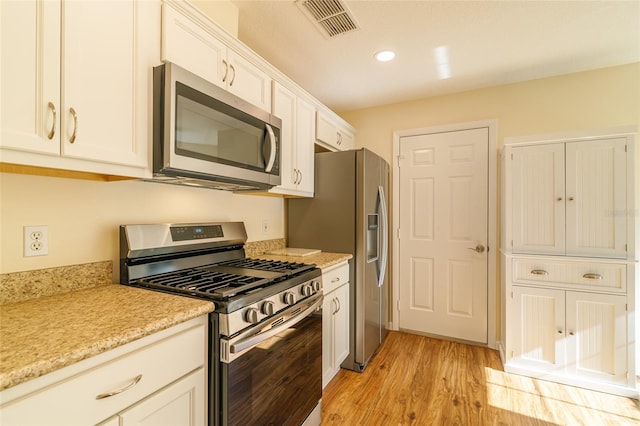 kitchen with stainless steel appliances, white cabinetry, and light hardwood / wood-style flooring