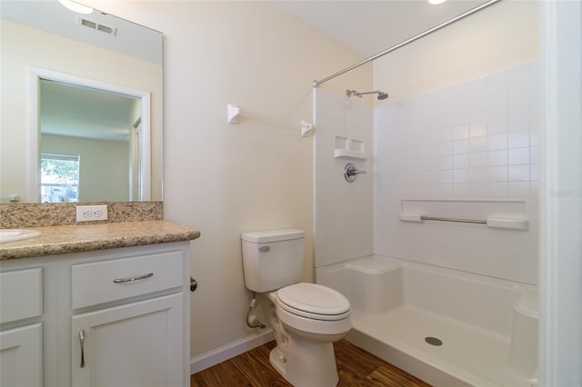 bathroom featuring wood-type flooring, vanity, a tile shower, and toilet