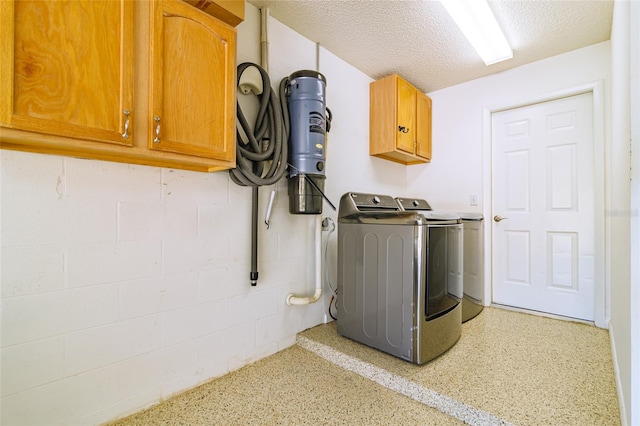 laundry room with a textured ceiling, washer and clothes dryer, and cabinets