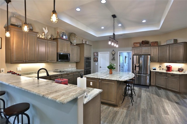 kitchen featuring a raised ceiling, a breakfast bar area, stainless steel appliances, a center island, and dark hardwood / wood-style floors