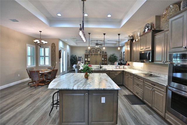 kitchen featuring wood-type flooring, a raised ceiling, hanging light fixtures, and a kitchen bar