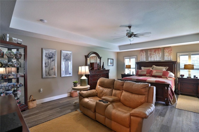 bedroom with a tray ceiling, ceiling fan, and dark wood-type flooring