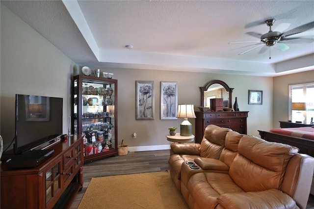 living room with a tray ceiling, dark hardwood / wood-style floors, and ceiling fan