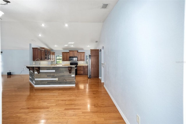 kitchen with light hardwood / wood-style floors, high vaulted ceiling, stainless steel appliances, and a breakfast bar area