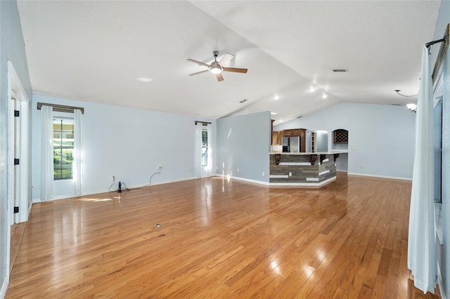 unfurnished living room with vaulted ceiling, ceiling fan with notable chandelier, and light hardwood / wood-style flooring