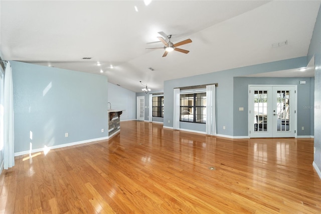 unfurnished living room with ceiling fan with notable chandelier, light hardwood / wood-style flooring, lofted ceiling, and french doors