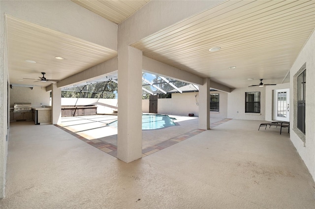 view of pool with grilling area, glass enclosure, ceiling fan, a patio area, and an outdoor kitchen