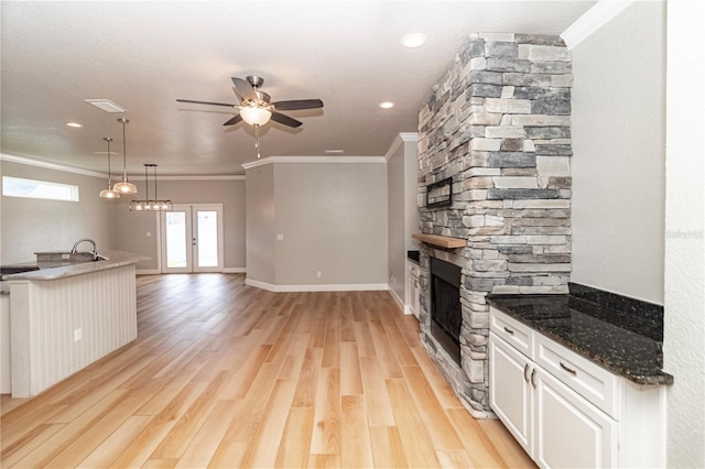 kitchen with dark stone counters, white cabinets, hanging light fixtures, light hardwood / wood-style flooring, and ornamental molding