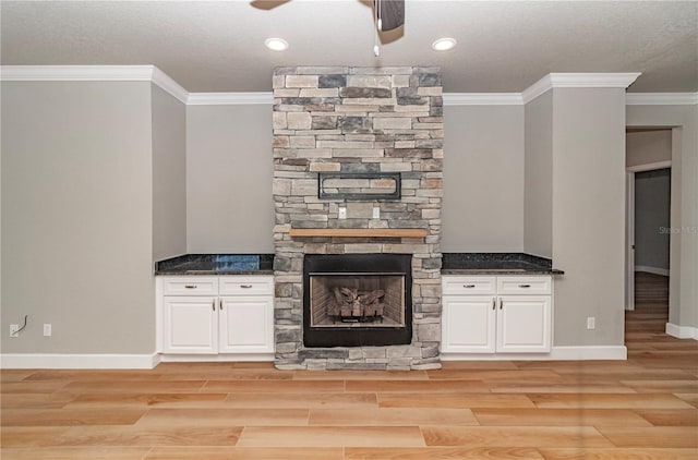 unfurnished living room featuring ornamental molding, a textured ceiling, light hardwood / wood-style floors, and a stone fireplace