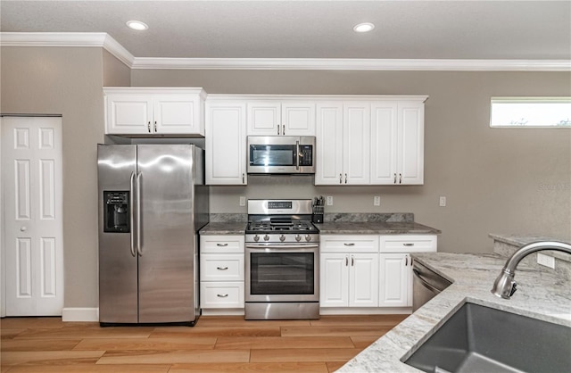 kitchen with sink, white cabinetry, light hardwood / wood-style flooring, appliances with stainless steel finishes, and light stone countertops