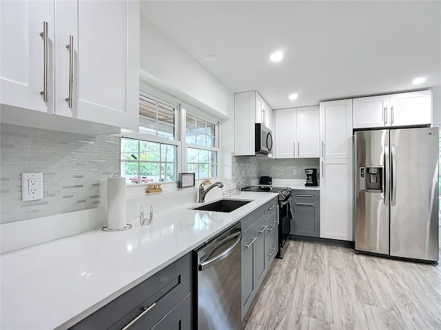 kitchen featuring appliances with stainless steel finishes, gray cabinetry, white cabinetry, light hardwood / wood-style flooring, and sink