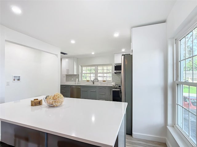 kitchen featuring light hardwood / wood-style floors, white cabinetry, tasteful backsplash, gray cabinets, and stainless steel appliances