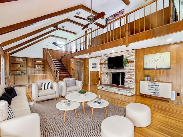 living room featuring a brick fireplace, high vaulted ceiling, beamed ceiling, light wood-type flooring, and wooden walls