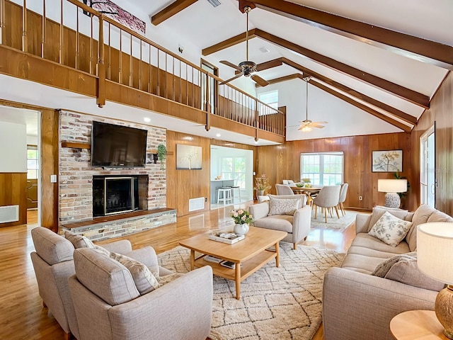 living room with light wood-type flooring, beamed ceiling, wood walls, a fireplace, and high vaulted ceiling