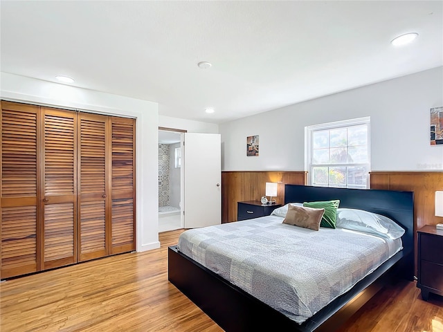 bedroom featuring ensuite bath, a closet, wood walls, and light hardwood / wood-style floors