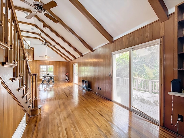 unfurnished living room with light wood-type flooring, wood walls, beam ceiling, and a wealth of natural light