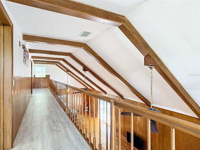 corridor with light hardwood / wood-style flooring, wooden walls, and vaulted ceiling with beams