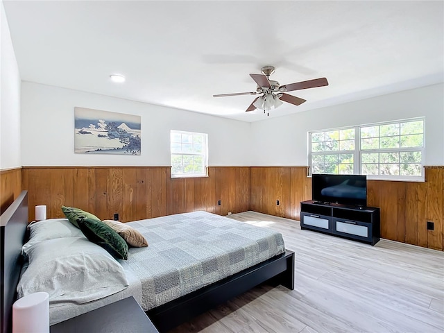 bedroom with ceiling fan, wooden walls, and light hardwood / wood-style flooring