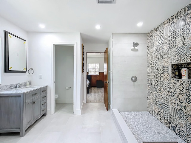 bathroom with a tile shower, tile walls, tile patterned floors, vanity, and toilet