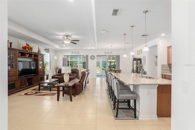 living room featuring ceiling fan with notable chandelier, a raised ceiling, sink, and light tile patterned floors