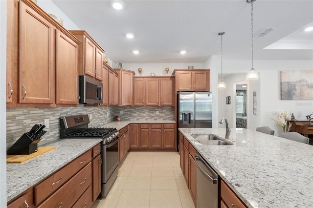 kitchen featuring sink, hanging light fixtures, stainless steel appliances, backsplash, and light stone countertops