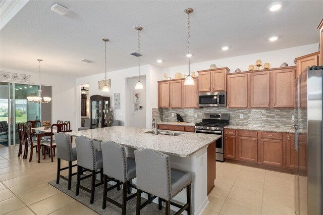 kitchen featuring an island with sink, appliances with stainless steel finishes, hanging light fixtures, and sink