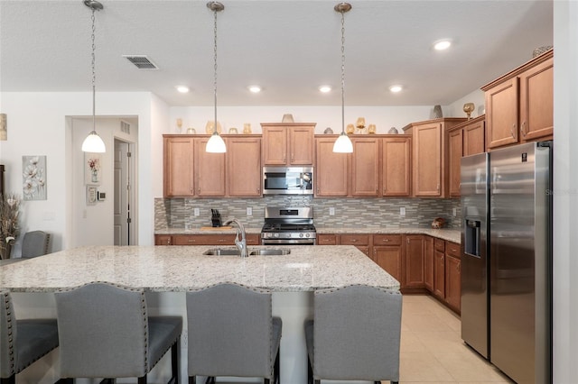 kitchen with appliances with stainless steel finishes, decorative light fixtures, an island with sink, sink, and a kitchen breakfast bar