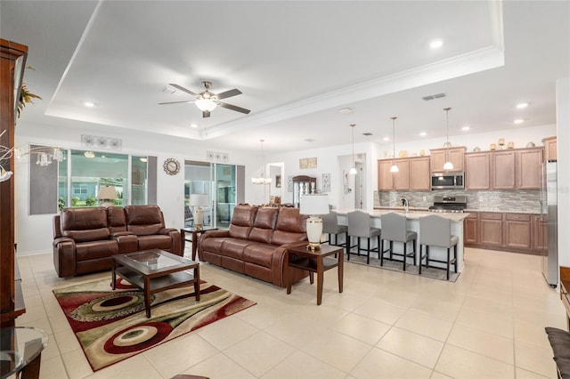 tiled living room featuring a raised ceiling, crown molding, and ceiling fan with notable chandelier