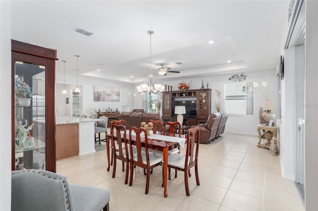 tiled dining space with ceiling fan and a raised ceiling