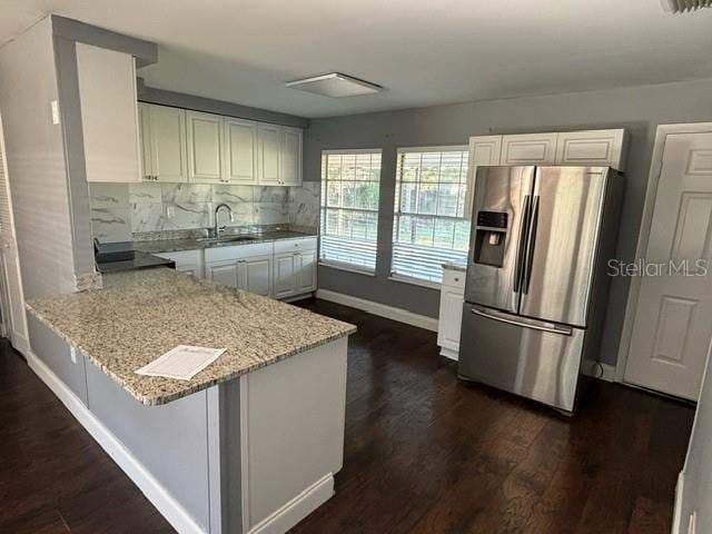 kitchen with light stone countertops, kitchen peninsula, a kitchen breakfast bar, white cabinetry, and stainless steel refrigerator with ice dispenser