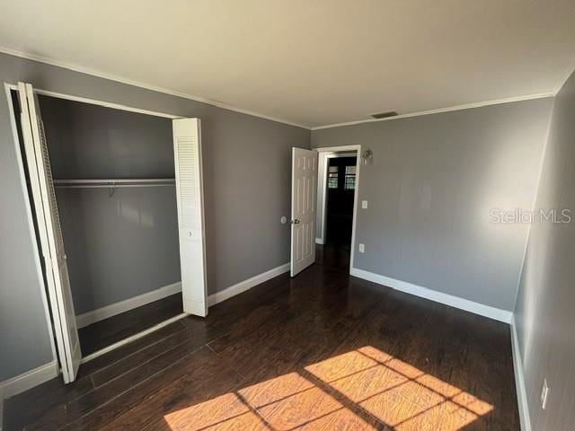 unfurnished bedroom featuring a closet, crown molding, and dark hardwood / wood-style flooring