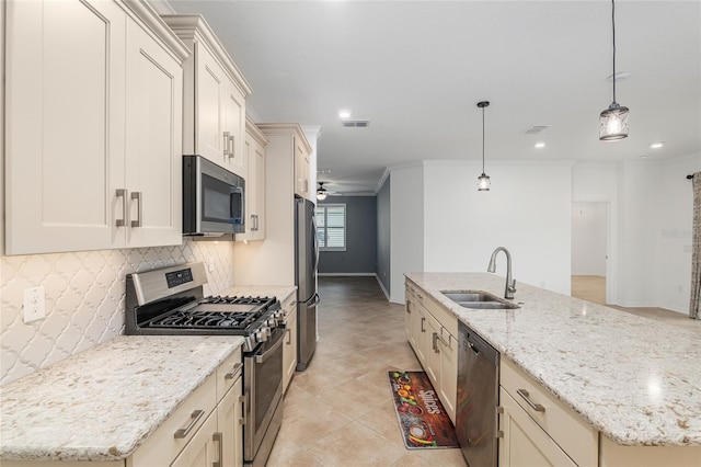 kitchen featuring light stone counters, an island with sink, sink, decorative light fixtures, and appliances with stainless steel finishes