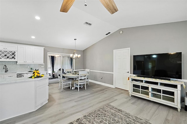 interior space featuring ceiling fan with notable chandelier, sink, white cabinets, and vaulted ceiling