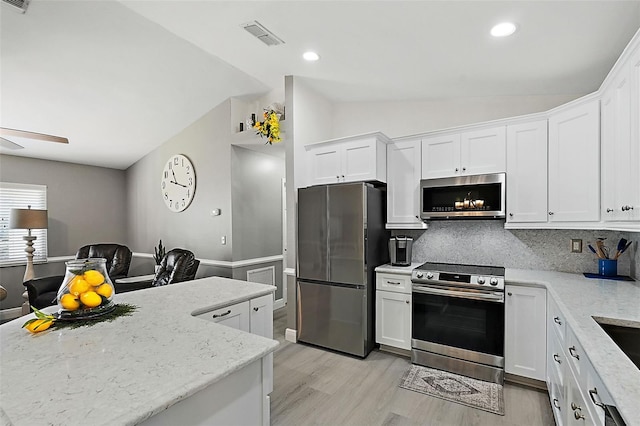 kitchen featuring white cabinets, decorative backsplash, stainless steel appliances, and vaulted ceiling