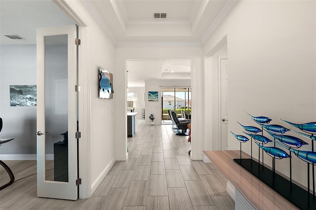 corridor with light hardwood / wood-style flooring, crown molding, and a tray ceiling