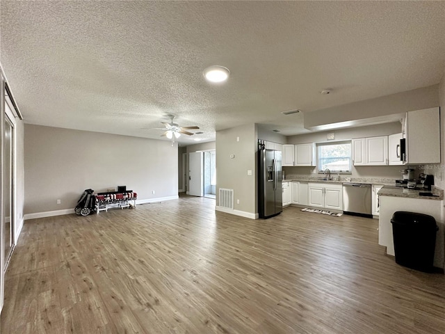 kitchen featuring light wood-type flooring, a textured ceiling, white cabinets, stainless steel appliances, and ceiling fan