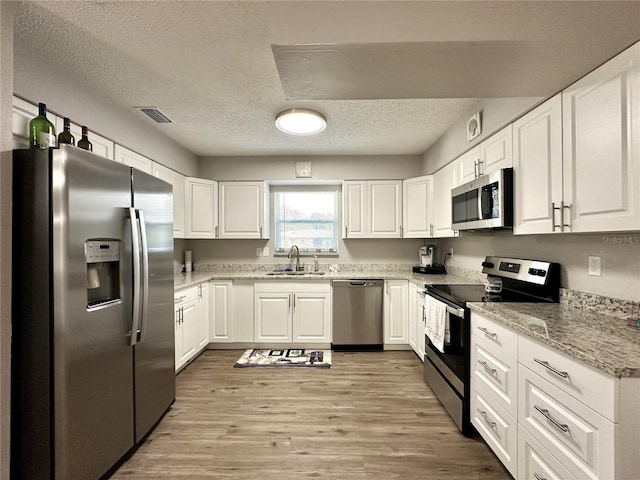 kitchen with appliances with stainless steel finishes, white cabinetry, sink, and light hardwood / wood-style flooring