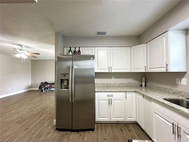 kitchen with stainless steel refrigerator with ice dispenser, white cabinetry, wood-type flooring, and light stone counters